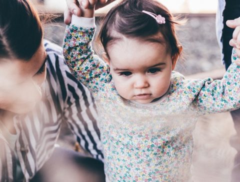 woman holding girl while learning to walk taken at daytime